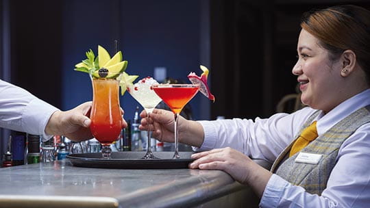 Cocktails being placed on a tray by staff in the North Cape Bar on Spirit of Adventure